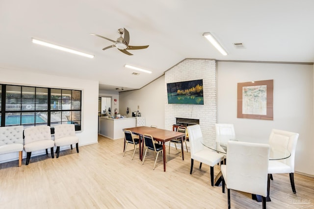 dining room featuring ceiling fan, light hardwood / wood-style floors, vaulted ceiling, and a brick fireplace