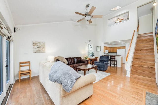 living room with ceiling fan, light hardwood / wood-style floors, ornamental molding, and a high ceiling