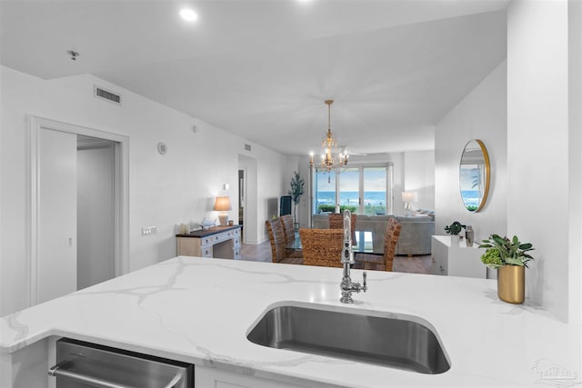 kitchen featuring light stone counters, visible vents, a sink, a notable chandelier, and open floor plan