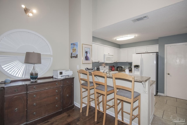 kitchen featuring white cabinetry, a breakfast bar area, dark brown cabinetry, kitchen peninsula, and white appliances