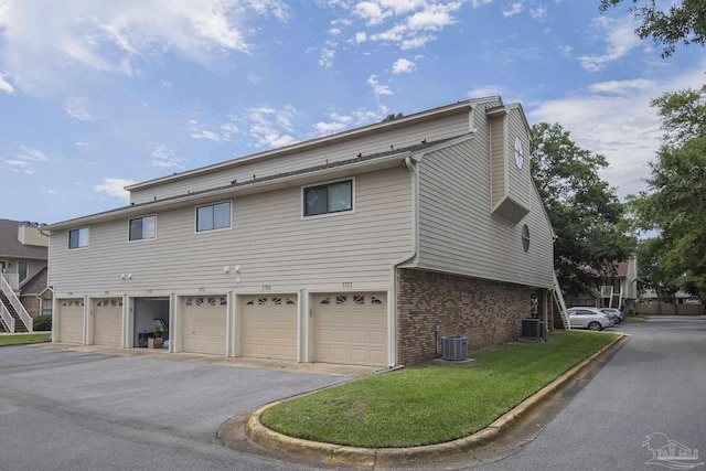 exterior space featuring a garage, cooling unit, and a lawn