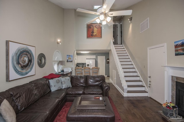 living room featuring ceiling fan, dark hardwood / wood-style flooring, a tiled fireplace, and a high ceiling