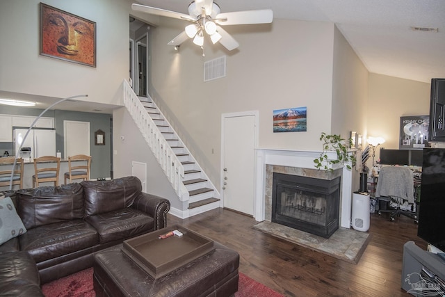 living room with dark wood-type flooring, ceiling fan, a tiled fireplace, and a high ceiling