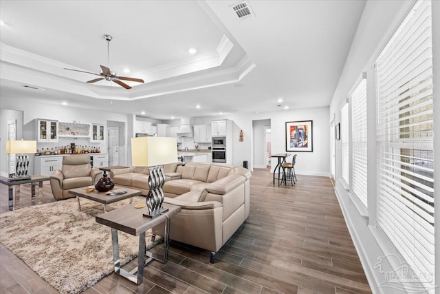 living area with a tray ceiling, a ceiling fan, recessed lighting, and a bar