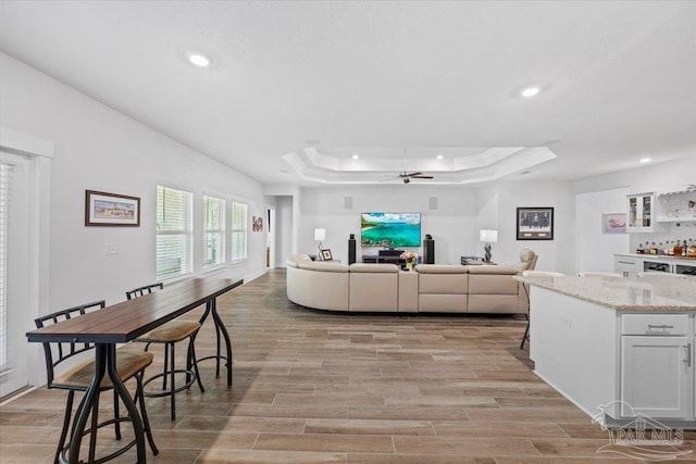 living room with a tray ceiling, light wood-style floors, a ceiling fan, and recessed lighting