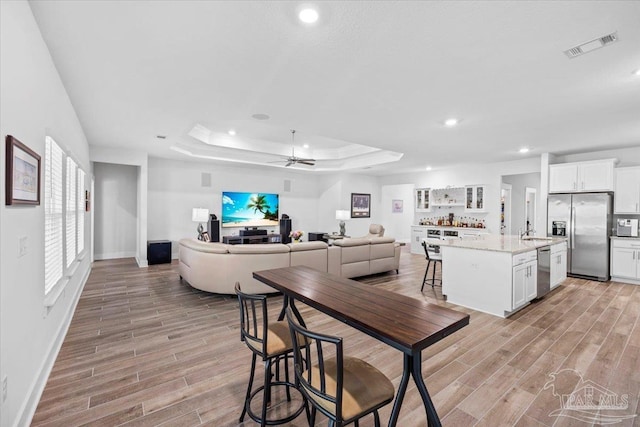 dining space featuring a tray ceiling, light wood-type flooring, baseboards, and recessed lighting