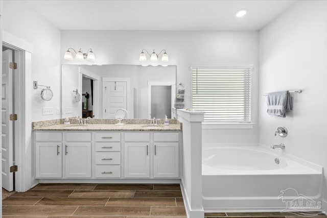 full bathroom with a bath, wood tiled floor, a sink, and double vanity