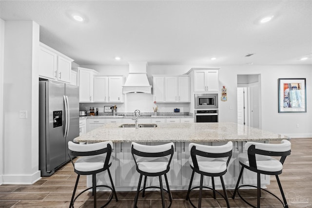 kitchen featuring stainless steel appliances, wood finished floors, baseboards, a kitchen island with sink, and custom exhaust hood