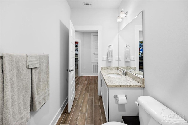 half bath with baseboards, toilet, wood finished floors, and visible vents