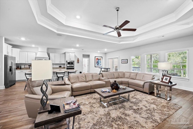 living area featuring wood finished floors, a ceiling fan, a tray ceiling, and ornamental molding
