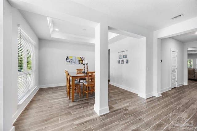 dining area featuring a raised ceiling, wood finished floors, visible vents, and baseboards