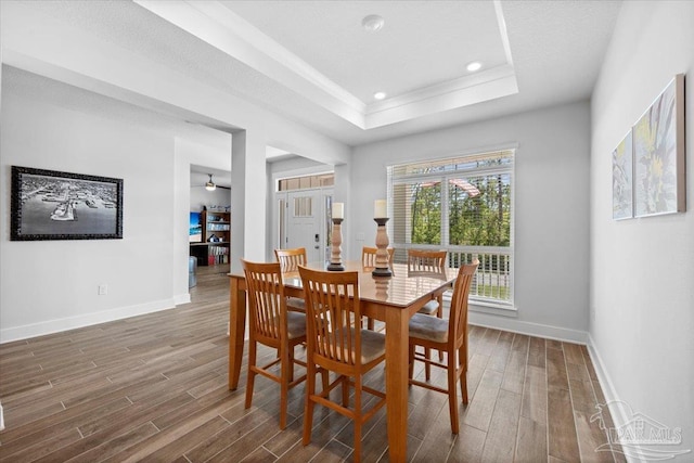 dining area with baseboards, a tray ceiling, and wood finished floors