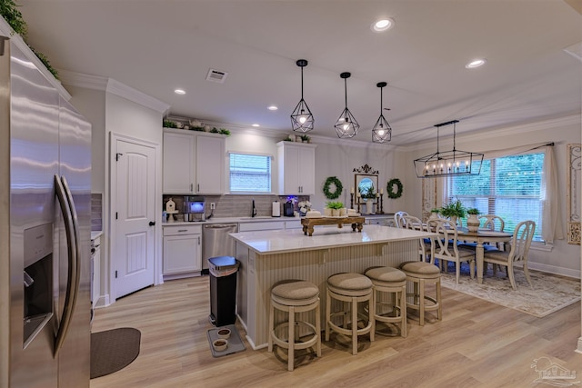 kitchen with a center island, appliances with stainless steel finishes, decorative light fixtures, light hardwood / wood-style floors, and white cabinetry