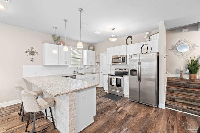 kitchen featuring a breakfast bar area, decorative light fixtures, kitchen peninsula, stainless steel appliances, and white cabinets