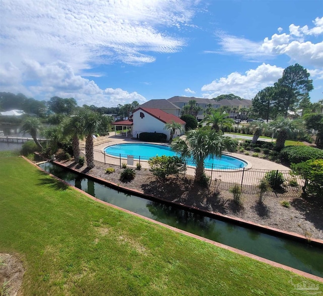 pool featuring a lawn, a water view, and fence