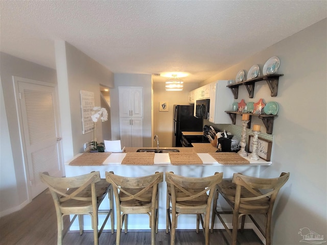 kitchen with white cabinets, a breakfast bar, a peninsula, black appliances, and a sink