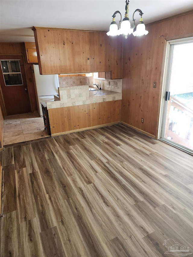 kitchen with sink, hanging light fixtures, an inviting chandelier, wood walls, and light wood-type flooring