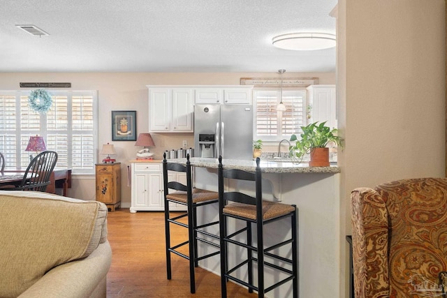 kitchen featuring white cabinetry, a kitchen breakfast bar, stainless steel refrigerator with ice dispenser, a textured ceiling, and light wood-type flooring