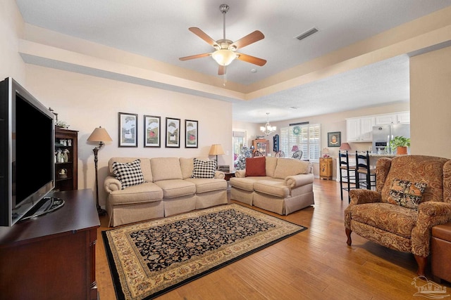 living room with ceiling fan with notable chandelier and light hardwood / wood-style floors