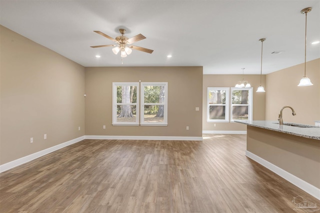 unfurnished living room featuring sink, ceiling fan with notable chandelier, wood-type flooring, and a healthy amount of sunlight