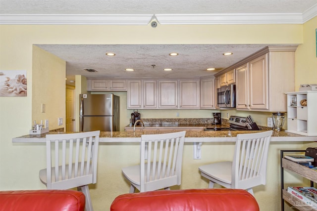 kitchen featuring a peninsula, appliances with stainless steel finishes, a textured ceiling, a kitchen bar, and crown molding