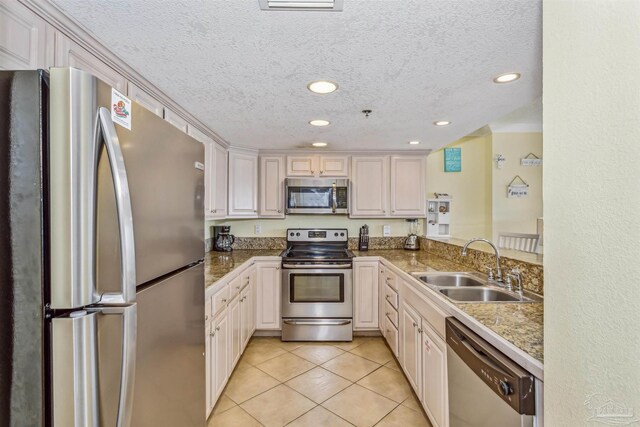 kitchen with a textured ceiling, light tile patterned flooring, appliances with stainless steel finishes, sink, and kitchen peninsula