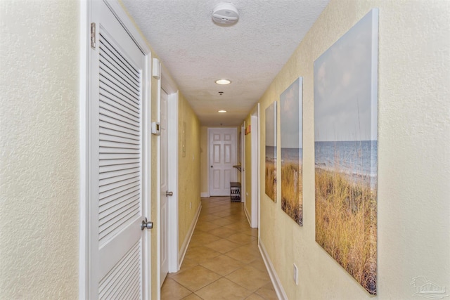 hall featuring baseboards, light tile patterned floors, recessed lighting, a textured wall, and a textured ceiling