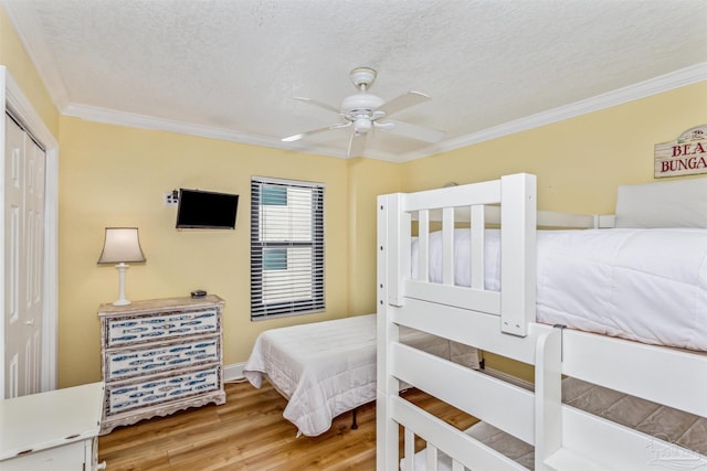 bedroom with a closet, a textured ceiling, wood finished floors, and ornamental molding