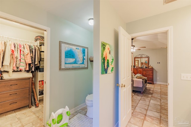 bathroom featuring baseboards, a ceiling fan, toilet, a walk in closet, and stone finish floor
