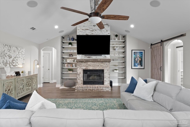 living room with lofted ceiling, wood-type flooring, a brick fireplace, ceiling fan, and a barn door