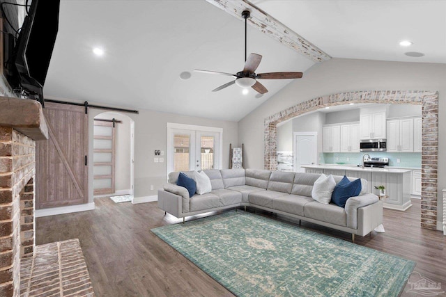 living room featuring dark wood-type flooring, french doors, lofted ceiling with beams, ceiling fan, and a barn door