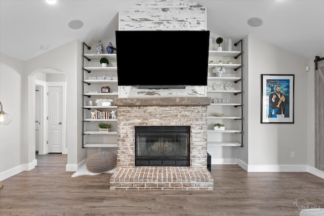 unfurnished living room featuring built in shelves, wood-type flooring, vaulted ceiling, a brick fireplace, and a barn door