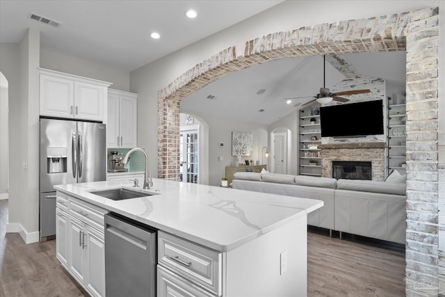 kitchen featuring sink, light stone counters, an island with sink, stainless steel appliances, and white cabinets