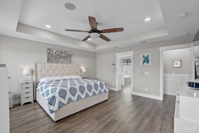 bedroom with ceiling fan, ensuite bathroom, a tray ceiling, and hardwood / wood-style floors