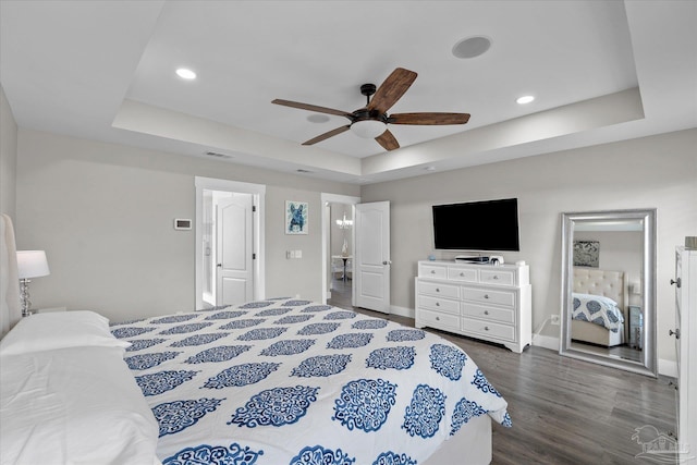 bedroom with dark wood-type flooring, ceiling fan, and a tray ceiling