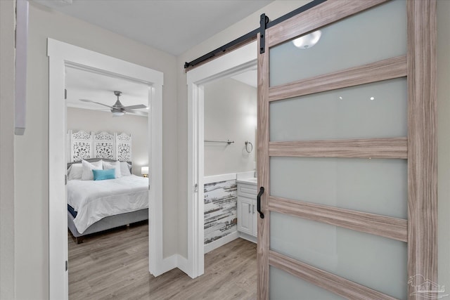 bedroom with a barn door, ceiling fan, and light wood-type flooring