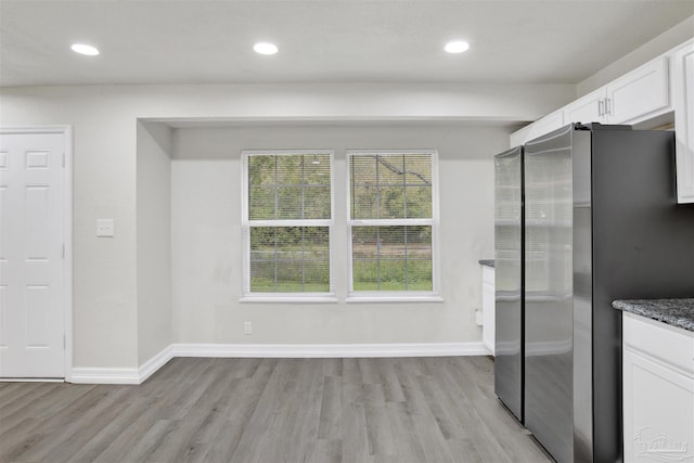 interior space with white cabinets, stainless steel fridge, light hardwood / wood-style flooring, and dark stone counters