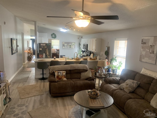 living room with a ceiling fan, baseboards, lofted ceiling, light wood-style floors, and a textured ceiling