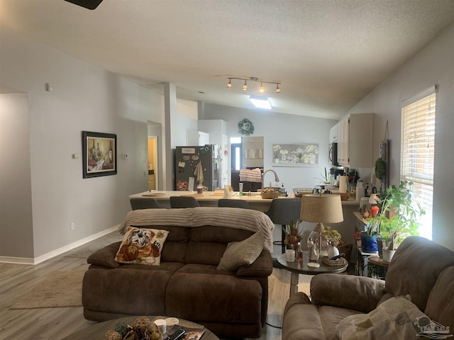 living area with vaulted ceiling, wood finished floors, baseboards, and a textured ceiling