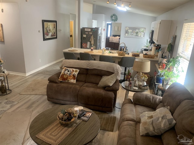 living room with baseboards, lofted ceiling, light wood-style flooring, and track lighting