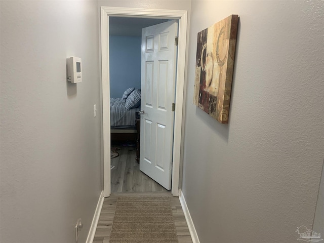 hall featuring a textured wall, baseboards, and wood finished floors