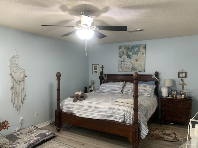 bedroom with visible vents, a textured ceiling, wood finished floors, baseboards, and ceiling fan