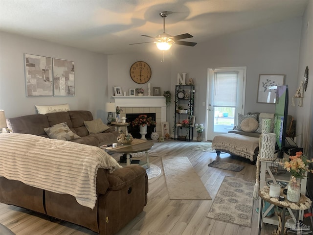 living room with a fireplace, light wood-type flooring, a ceiling fan, and vaulted ceiling