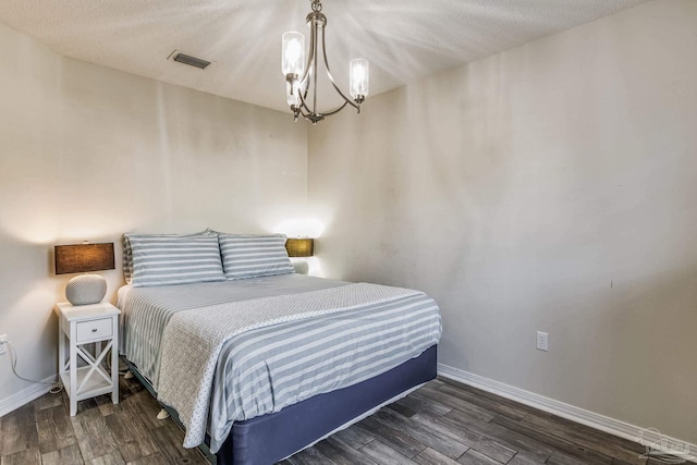 bedroom with dark hardwood / wood-style flooring, a textured ceiling, and a notable chandelier