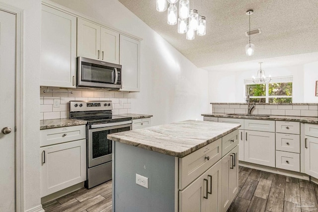 kitchen featuring appliances with stainless steel finishes, a textured ceiling, sink, hardwood / wood-style flooring, and a center island