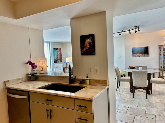 kitchen with a sink, light stone countertops, rail lighting, stone tile flooring, and stainless steel dishwasher