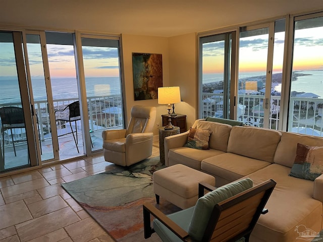 living room with stone tile floors, a water view, and floor to ceiling windows