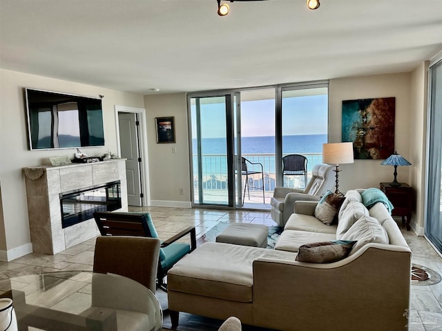 living area featuring baseboards, a water view, a tile fireplace, and floor to ceiling windows