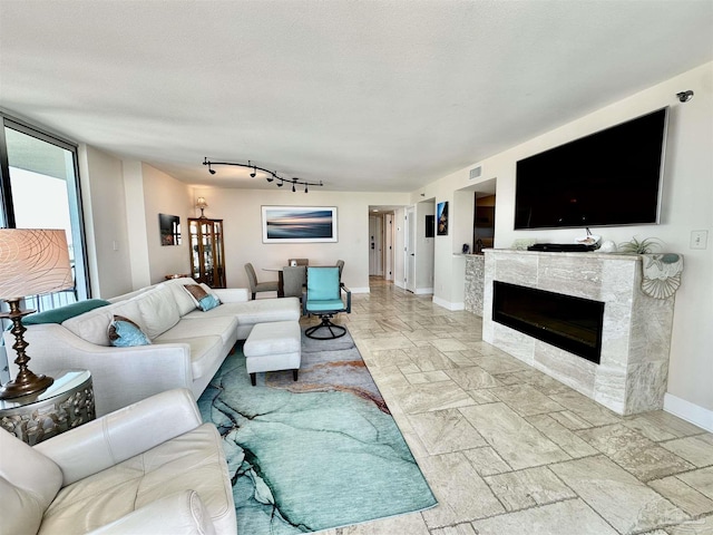 living room with a glass covered fireplace, visible vents, a textured ceiling, and baseboards