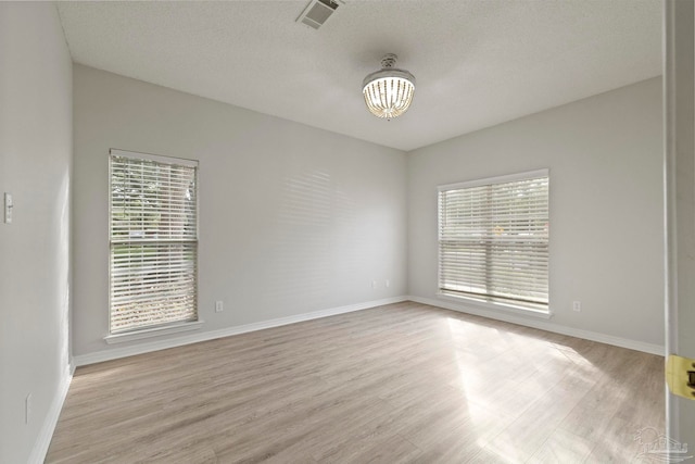 empty room with light hardwood / wood-style floors, a textured ceiling, and a notable chandelier